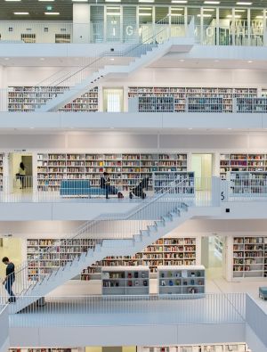interior d'una biblioteca moderna terra i escales blanques, prestatgeries de llibres a les parets i sofàs de color blau amb gent llegint